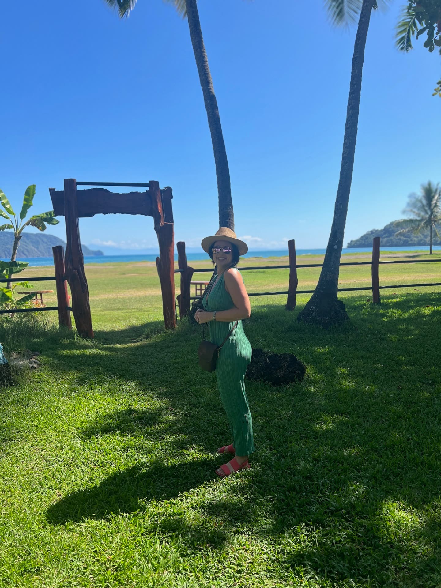 Blythe Milligan standing on a grassy shoreline with palm trees and the ocean behind her